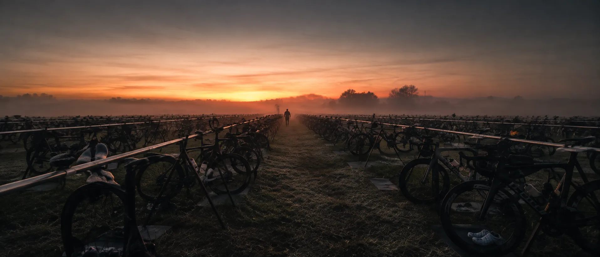 An empty race transition area at dawn, rows of racked bikes in mist